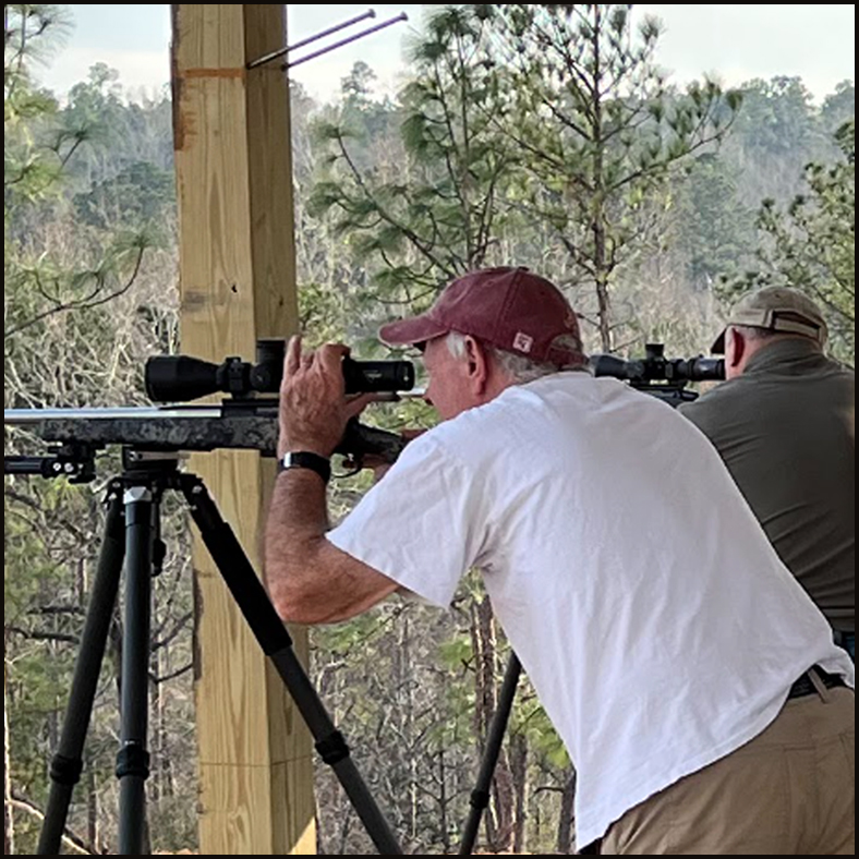 A man in a white tshirt looking into the sniper lens