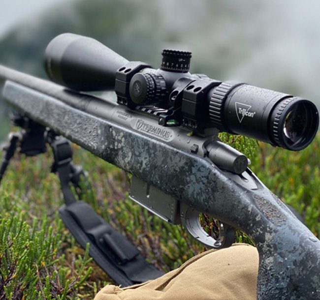 A rifle with a scope and bag in the grass.